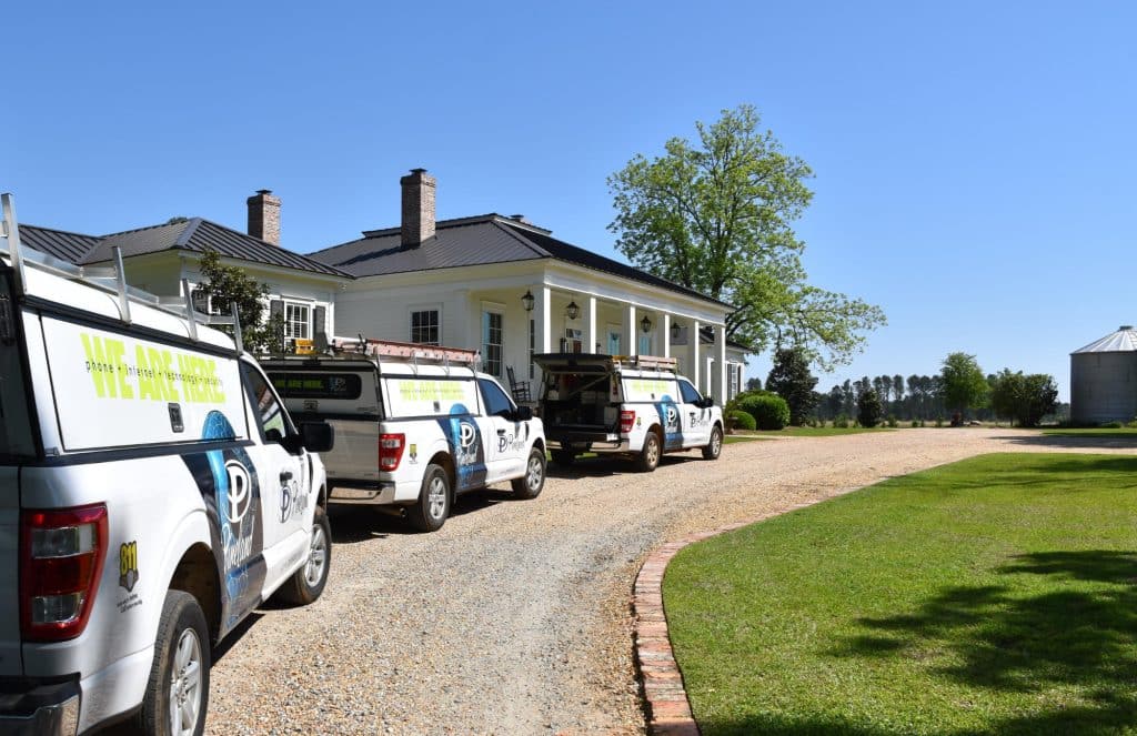 A line of three Pineland service trucks lined up in front of a customer's house.